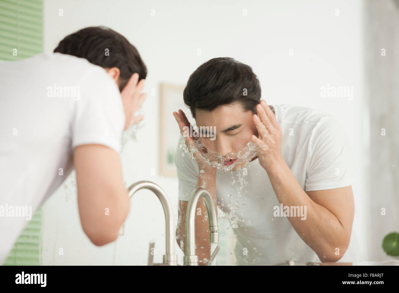 Porträt des jungen Mannes sein Gesicht am Waschbecken im Bad waschen Stockfoto