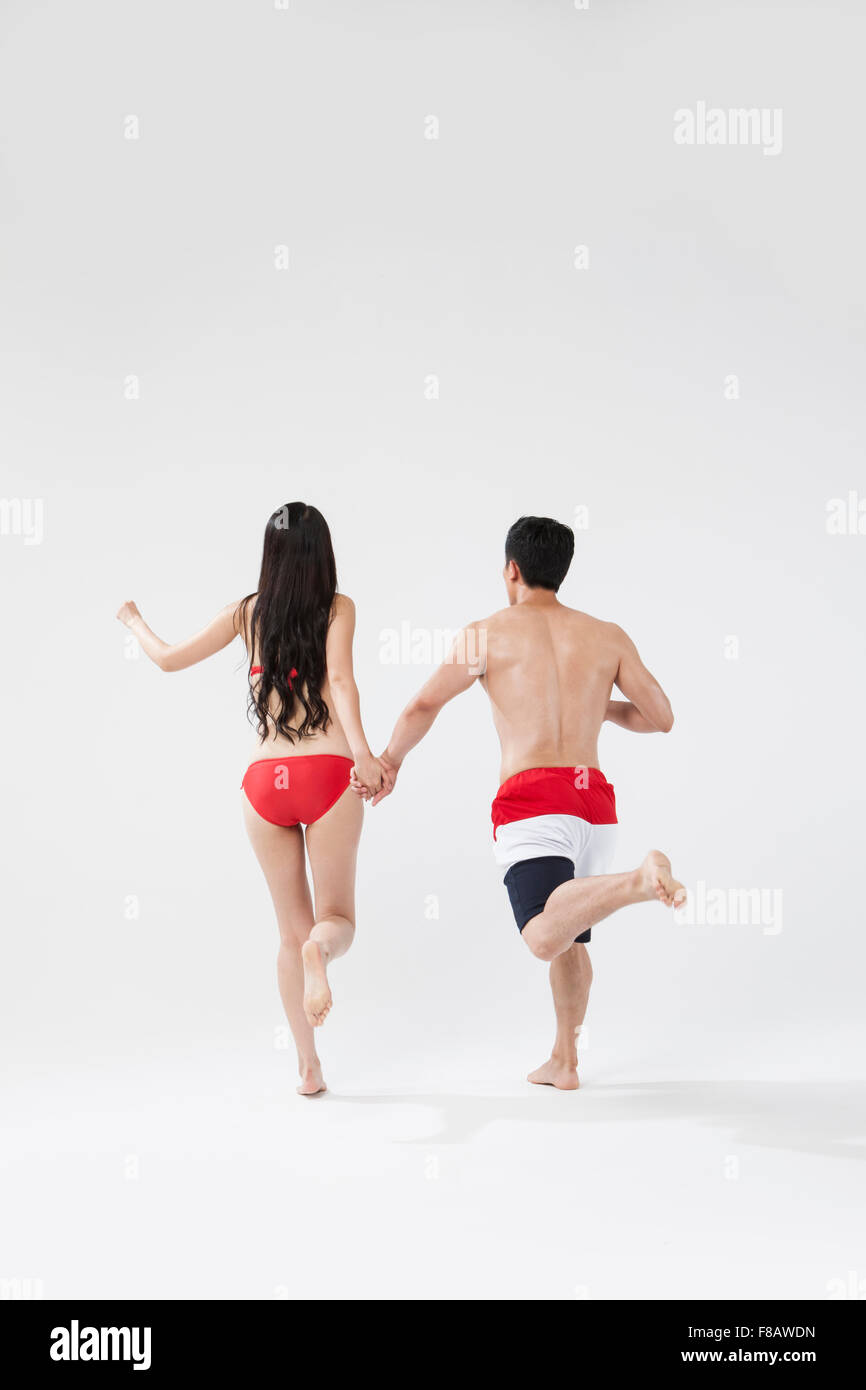 Rücken des Paares in Badeanzügen laufen hand in hand Stockfoto
