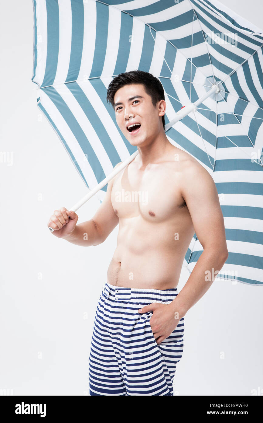 Mann im Badeanzug hält einen Sonnenschirm mit einem Lächeln legte Hand in der Tasche Stockfoto