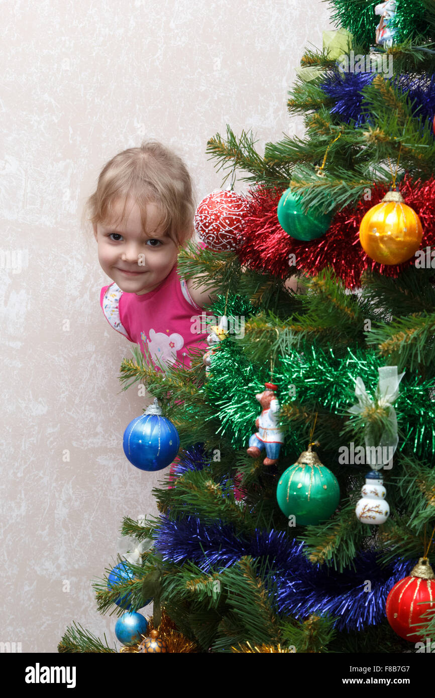 kleine Mädchen spähen heraus von hinten den Weihnachtsbaum Stockfoto