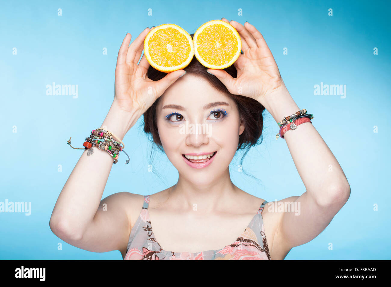 Frau hält Orangenscheiben über ihren Kopf mit einem Lächeln und auf der Suche zur Seite Stockfoto