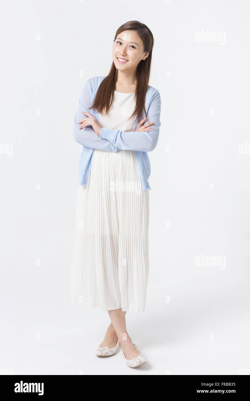 Koreanische Frau im weißen Kleid und blaue Strickjacke mit langen glatten Haaren stehen und lächelnd nach vorne Stockfoto