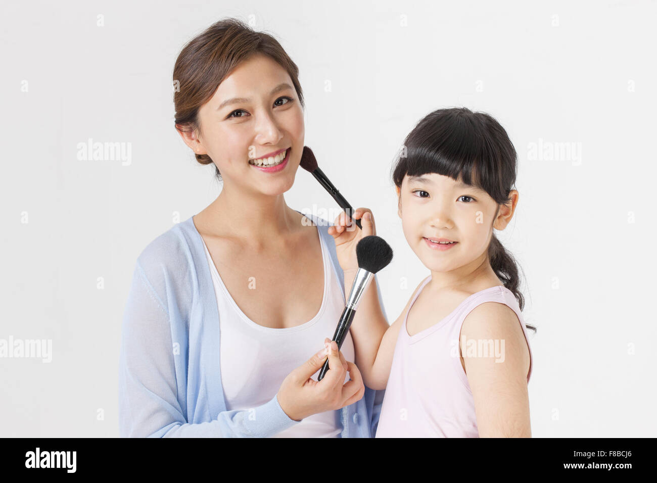 Mutter und Tochter hält Make-up Pinsel in der Nähe von einander ins Gesicht und beide starren vorwärts mit einem Lächeln Stockfoto