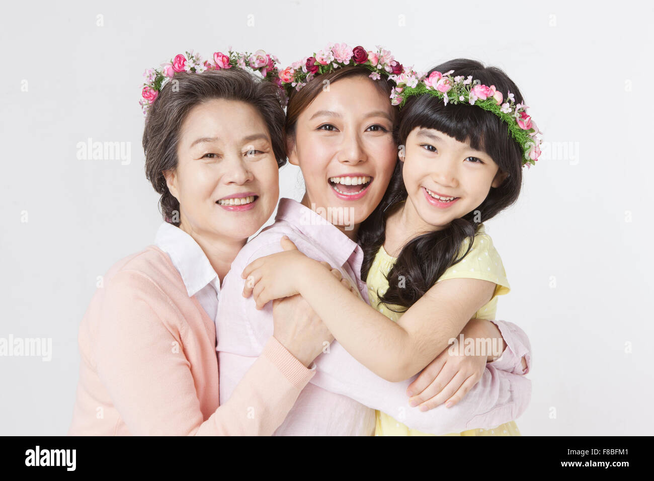 Mutter, Tochter, Großmutter umarmten einander und lächelnd nach vorne mit Blume Kronen auf dem Kopf Stockfoto