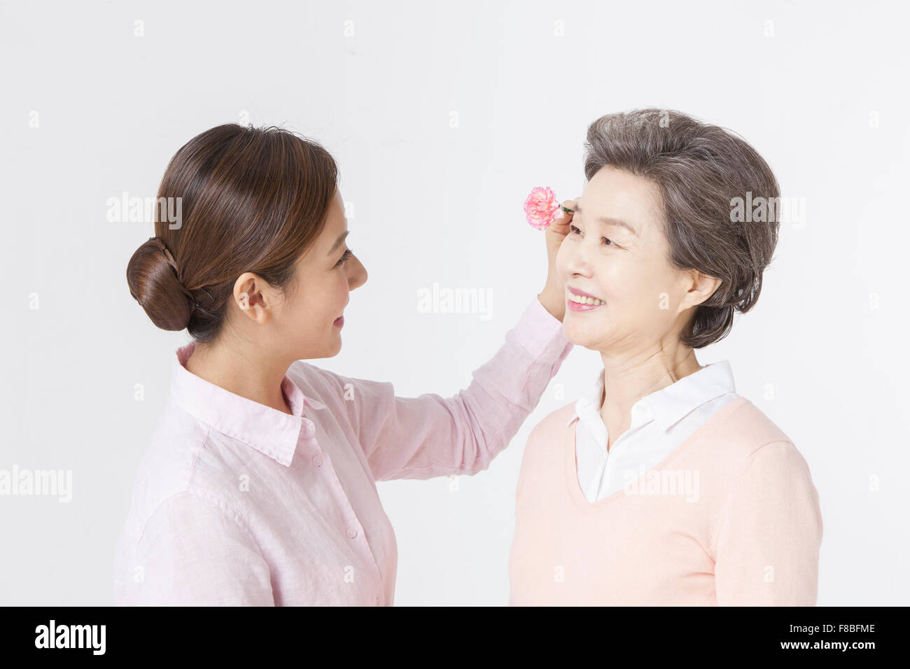 Tochter setzen eine Nelke Blume auf Mutters Ohr beide sahen einander Stockfoto