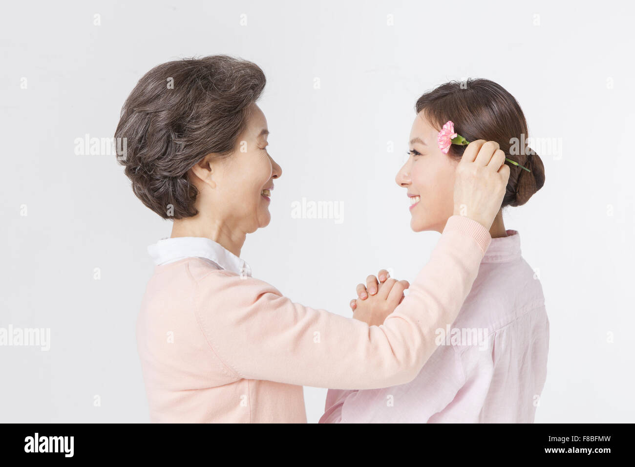 Mutter setzen eine Nelke Blume auf ihre Tochter Ohr beide sahen einander mit einem Lächeln Stockfoto