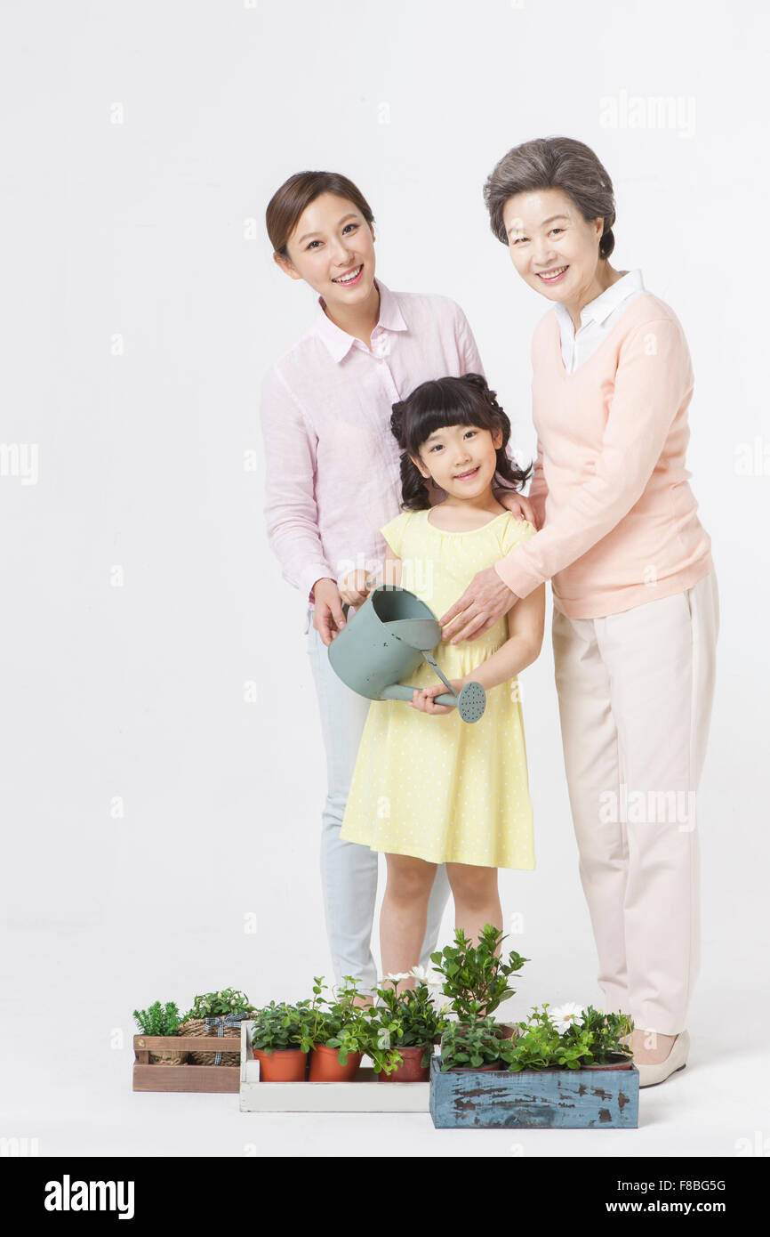 Großmutter, Mutter und Tochter Bewässerung der Pflanzen auf dem Boden alle starr nach vorn und lächelnd Stockfoto
