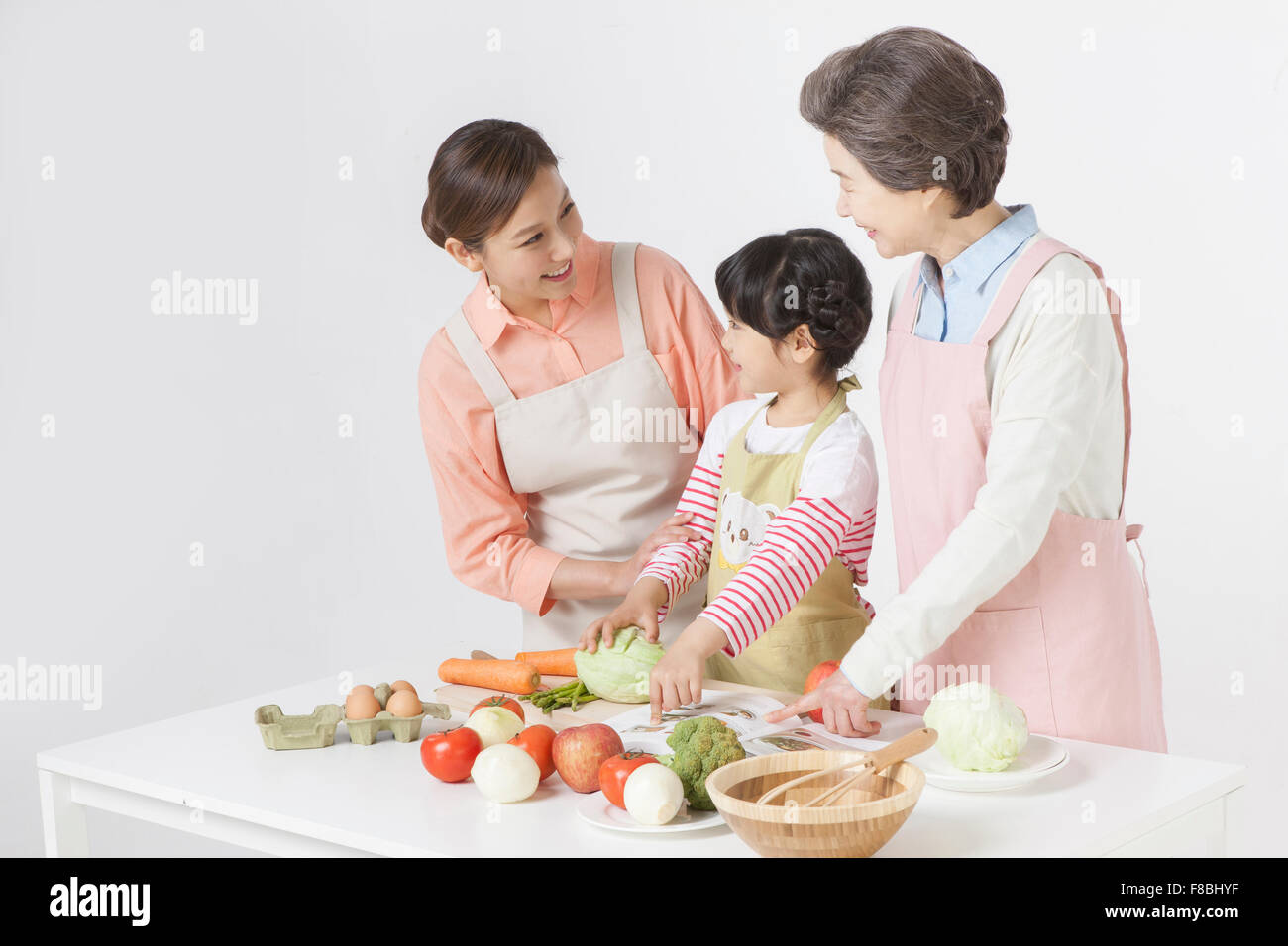 Rezeptbuch wies Tochter und Großmutter und Mutter Tochter und Großmutter alles in Schürze und gemeinsames Kochen Stockfoto