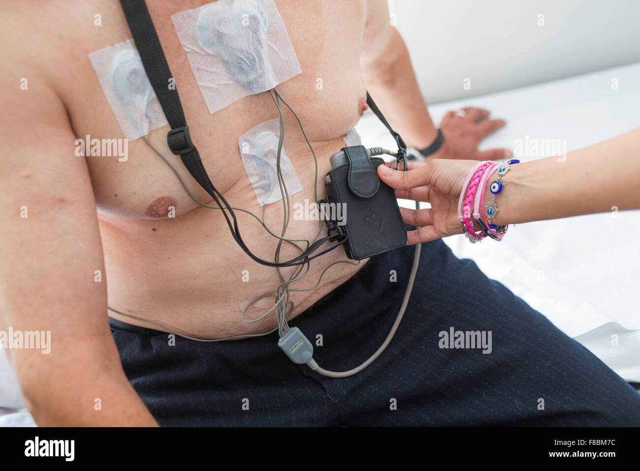 Platzieren die Elektroden auf die Brust eines männlichen Patienten, verbunden mit einer Holter-Monitor an ihrer Taille. Ein Holter-Monitor ist ein tragbares EKG (ECG) Gerät. Es kann messen und aufzeichnen die elektrische Aktivität des Herzens des Patienten über 24 Stunden und erkennen Stockfoto