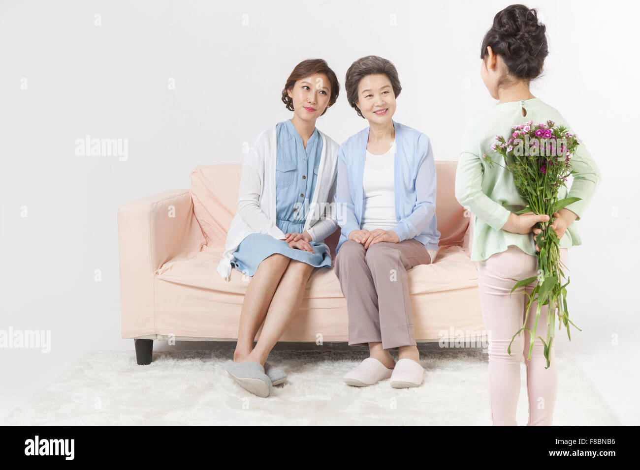 Mutter und Tochter sitzen auf einem Sofa und Blick auf die Enkelin Blumen hinter ihrem Rücken versteckt Stockfoto