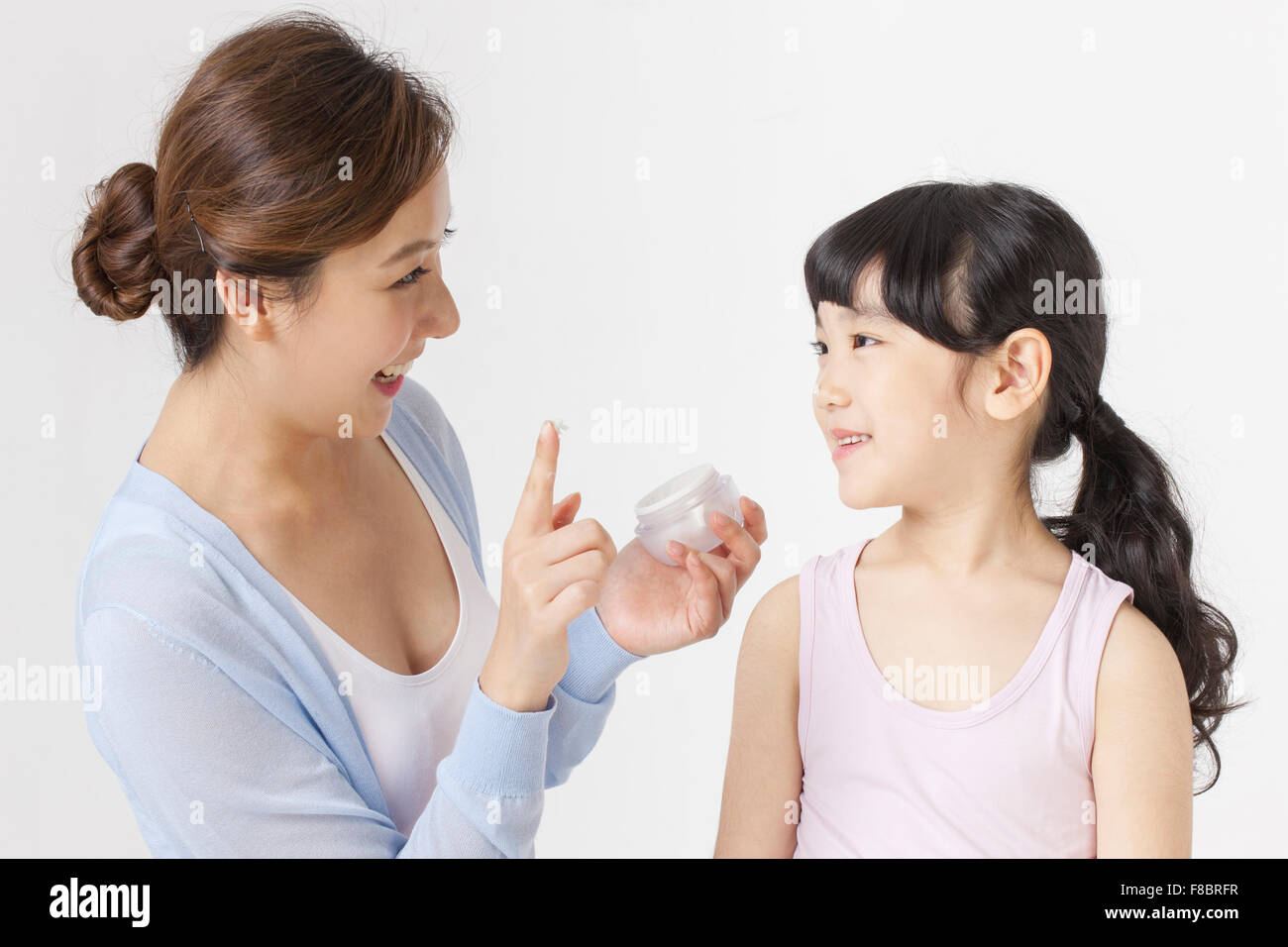 Mutter hält eine Gesichtscreme, auf ihre Tochter Gesicht gelten beide sahen einander mit einem Lächeln Stockfoto