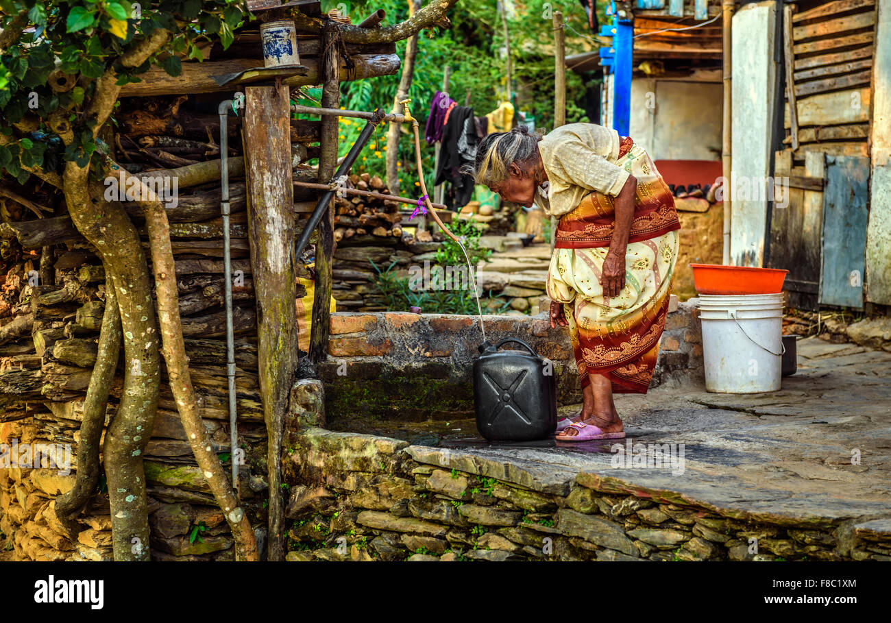 Sehr alte Frau gebeugt füllt ein Kanister mit Wasser. Stockfoto