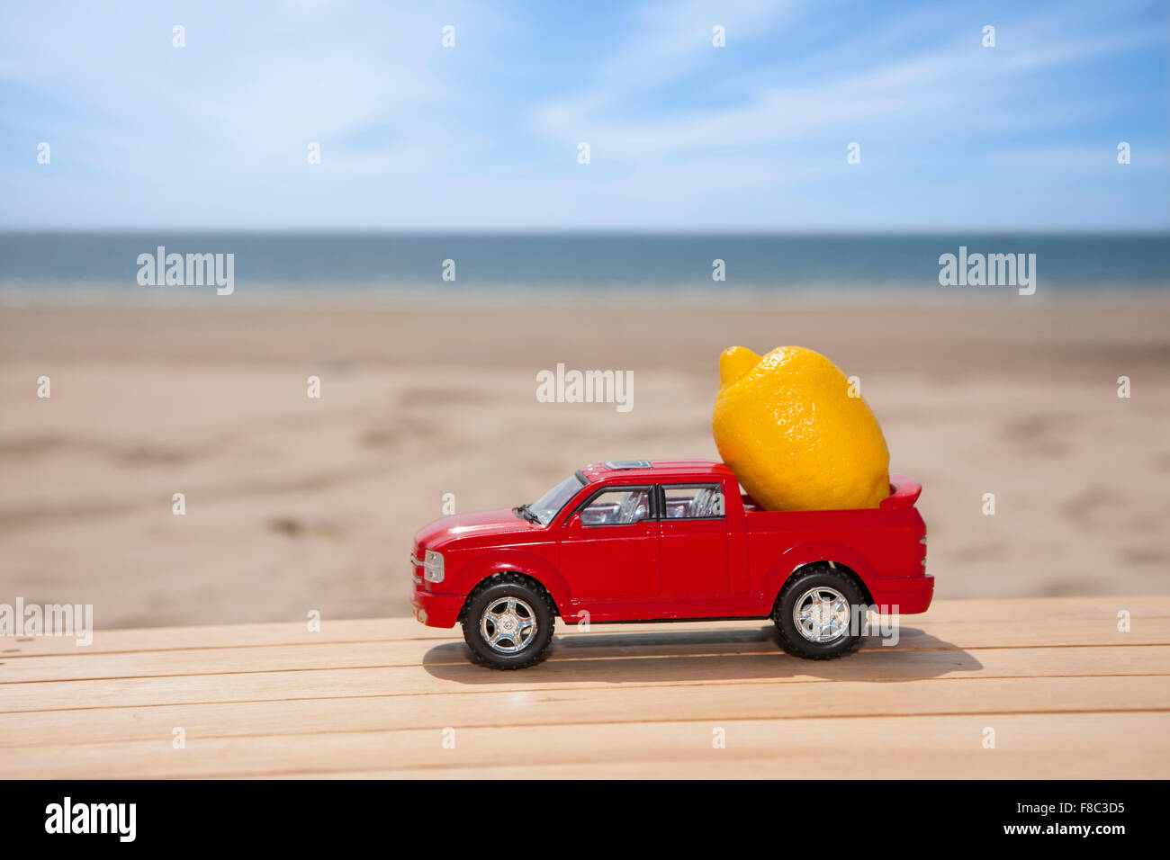 Miniatur-Wagen mit einer Zitrone auf Holzwerkstoff mit dem Hintergrund des Strandes Stockfoto