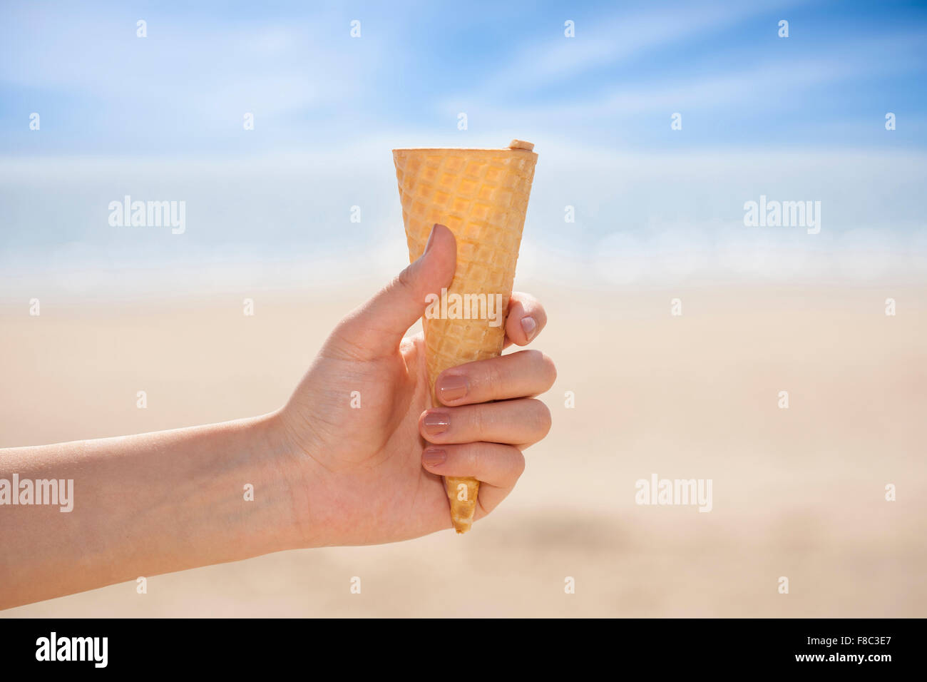 Eiswaffel ohne Eis statt von einer Hand aus dem Fokus mit dem Hintergrund des Strandes Stockfoto