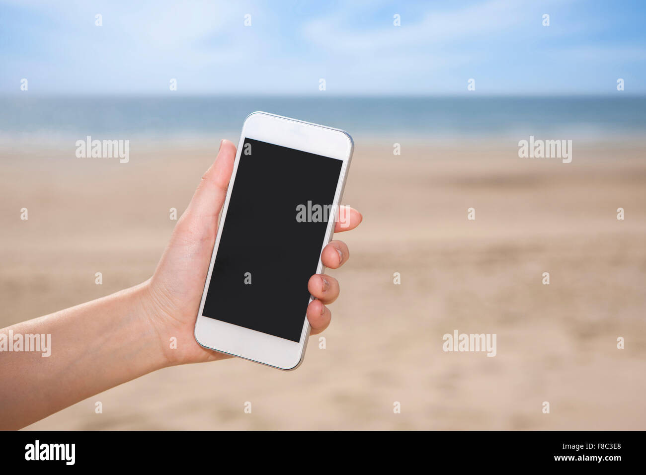 Smartphone statt von einer Hand aus dem Fokus mit dem Hintergrund des Strandes Stockfoto