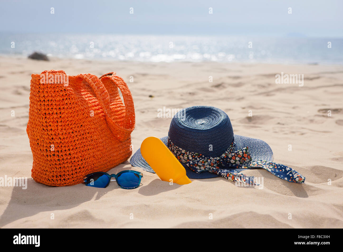 Tasche, Hut, Sonnencreme und Sonnenbrille auf Sand vor dem Hintergrund der Strand außerhalb des Fokus Stockfoto