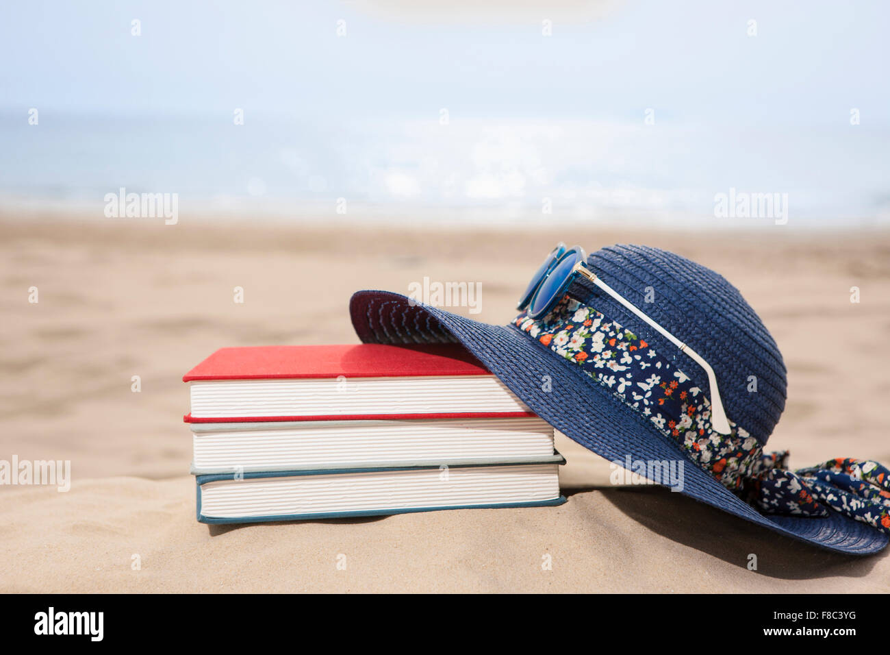 Hut und Bücher auf Sand aus dem Fokus mit dem Hintergrund des Strandes Stockfoto