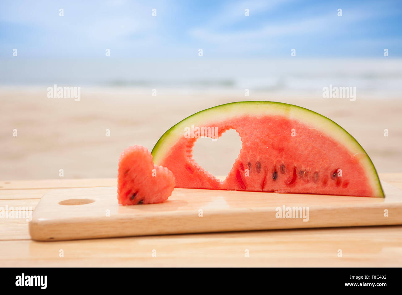 Wassermelone Stück geschnitzt in Herzform auf Schneidebrett aus dem Fokus mit dem Hintergrund des Strandes Stockfoto