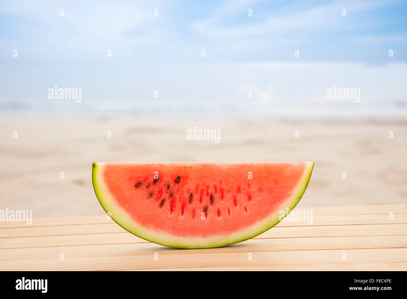 Wassermelone Stück auf Holzwerkstoff mit dem Hintergrund unscharf vom Strand Stockfoto