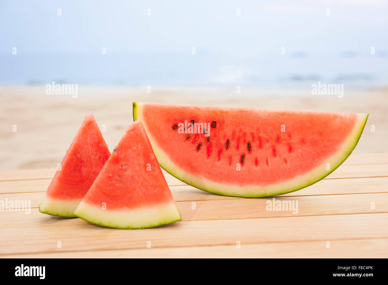 Wassermelone-Scheiben auf Holzwerkstoff mit dem Hintergrund des Strandes Stockfoto