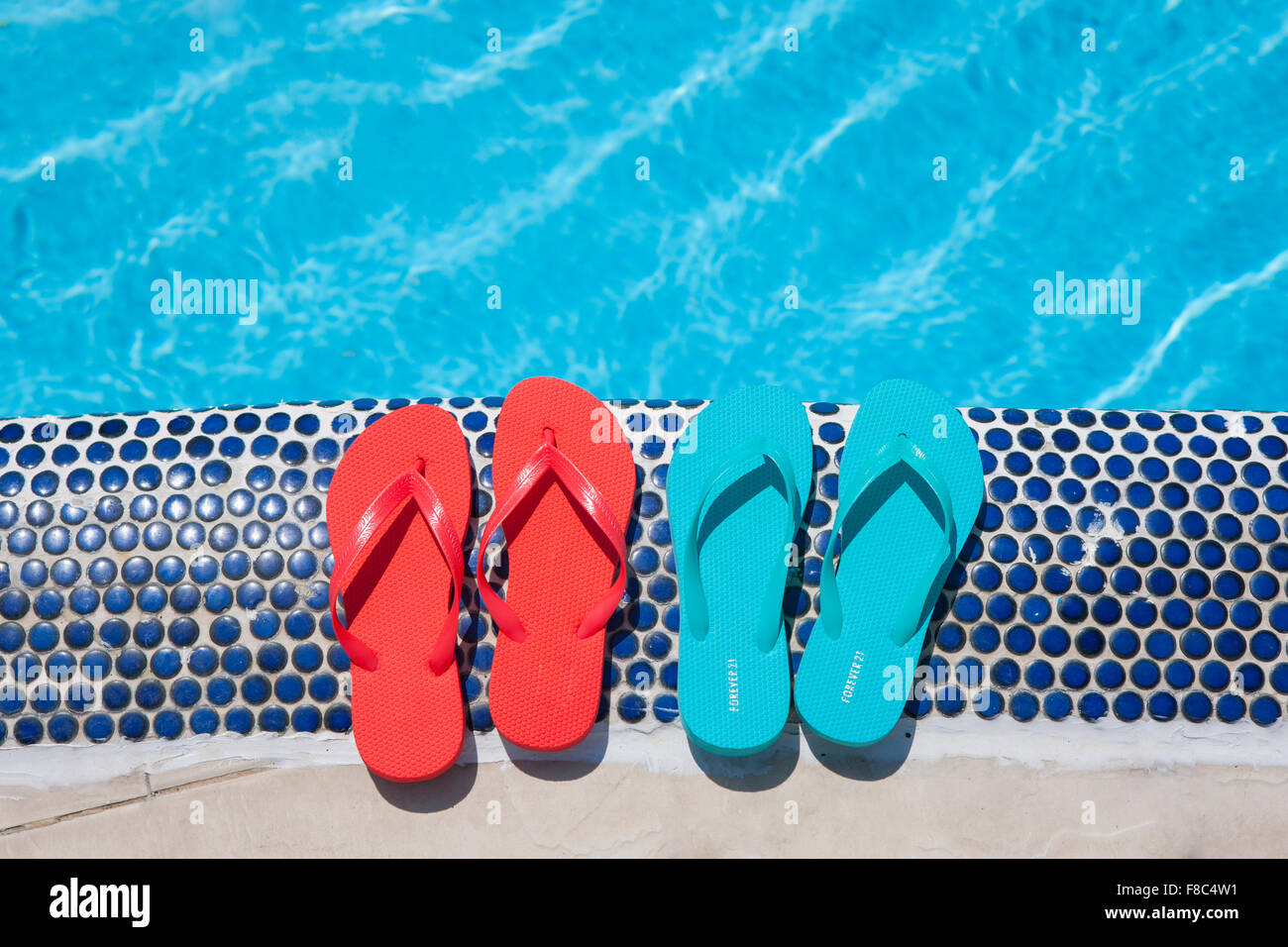Hohen Winkel von zwei Paaren von Flip flops am Rand des Swimmingpools Stockfoto