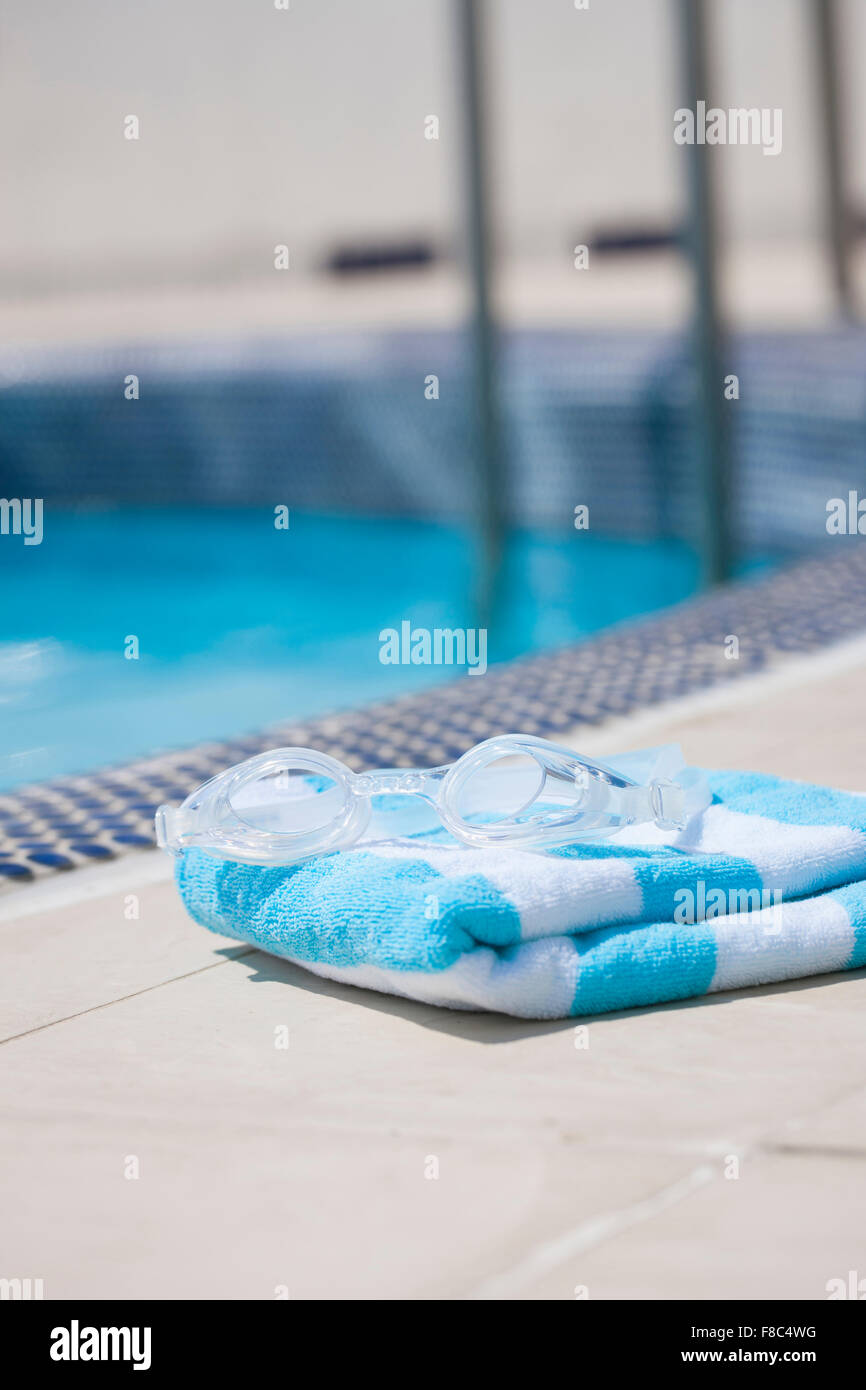 Schwimmbrille auf gefaltetes Handtuch außerhalb des Fokus mit dem Hintergrund der Swimmingpool Stockfoto