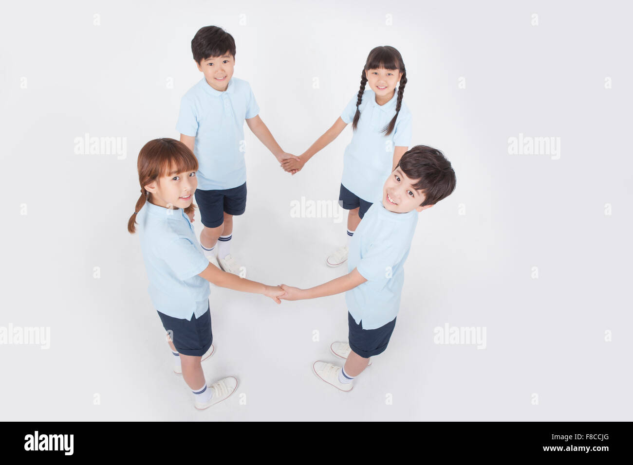 Hohen Winkel von vier Grundschüler im Sport Uniformen halten einander die Hände und stehen in einem Kreis Stockfoto