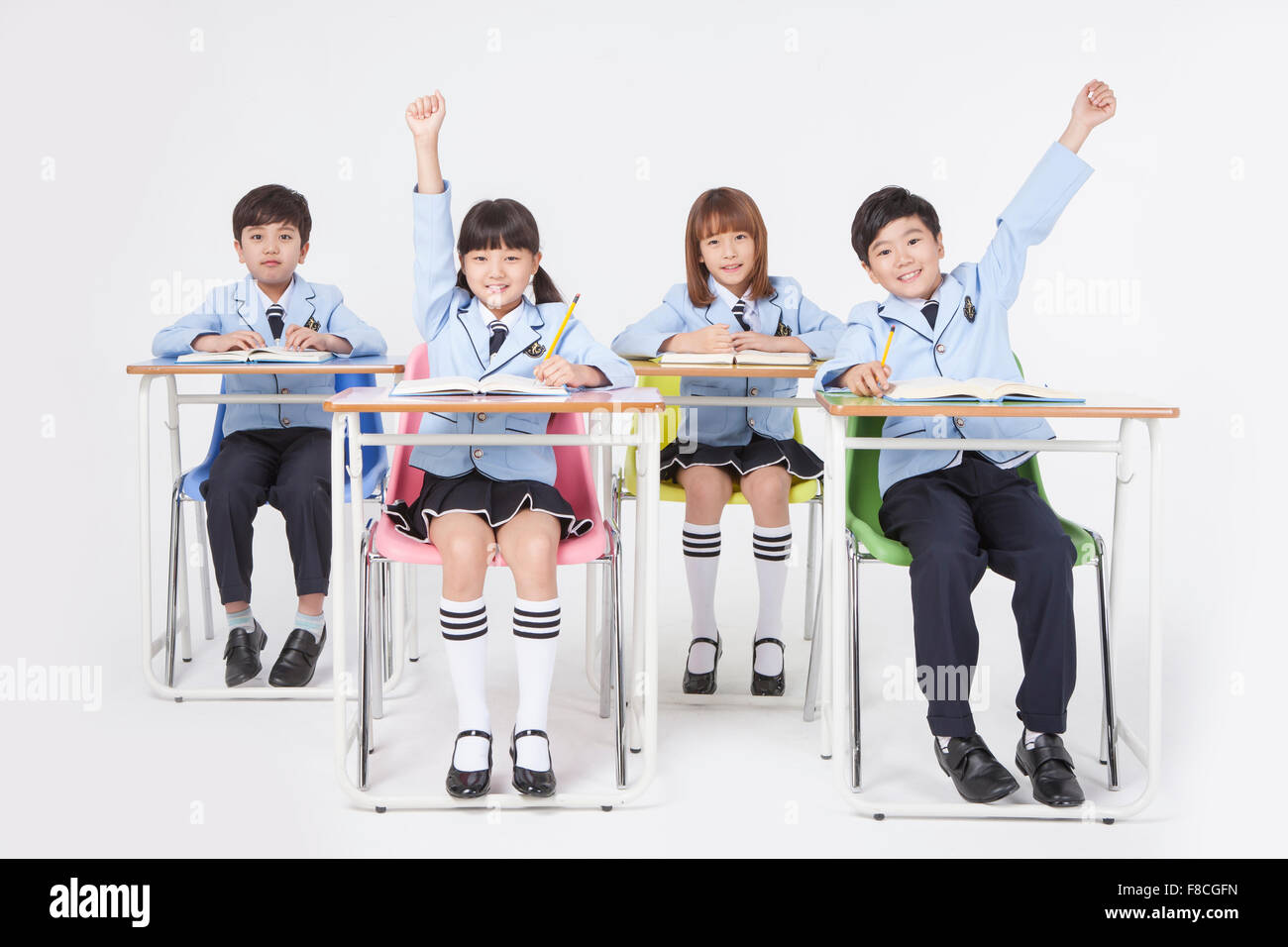 Vier Grundschüler in Schuluniformen sitzen am Schreibtisch studieren mit gelben Bleistifte und starrte nach vorne mit einem Lächeln Stockfoto