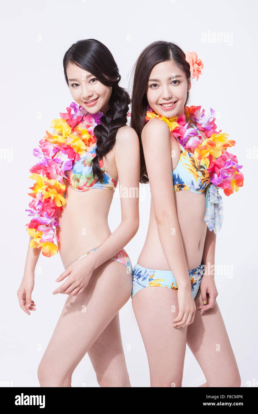 Zwei Frauen in Bikini und Blume Halskette Rücken an Rücken und starrte nach vorne mit einem Lächeln Stockfoto