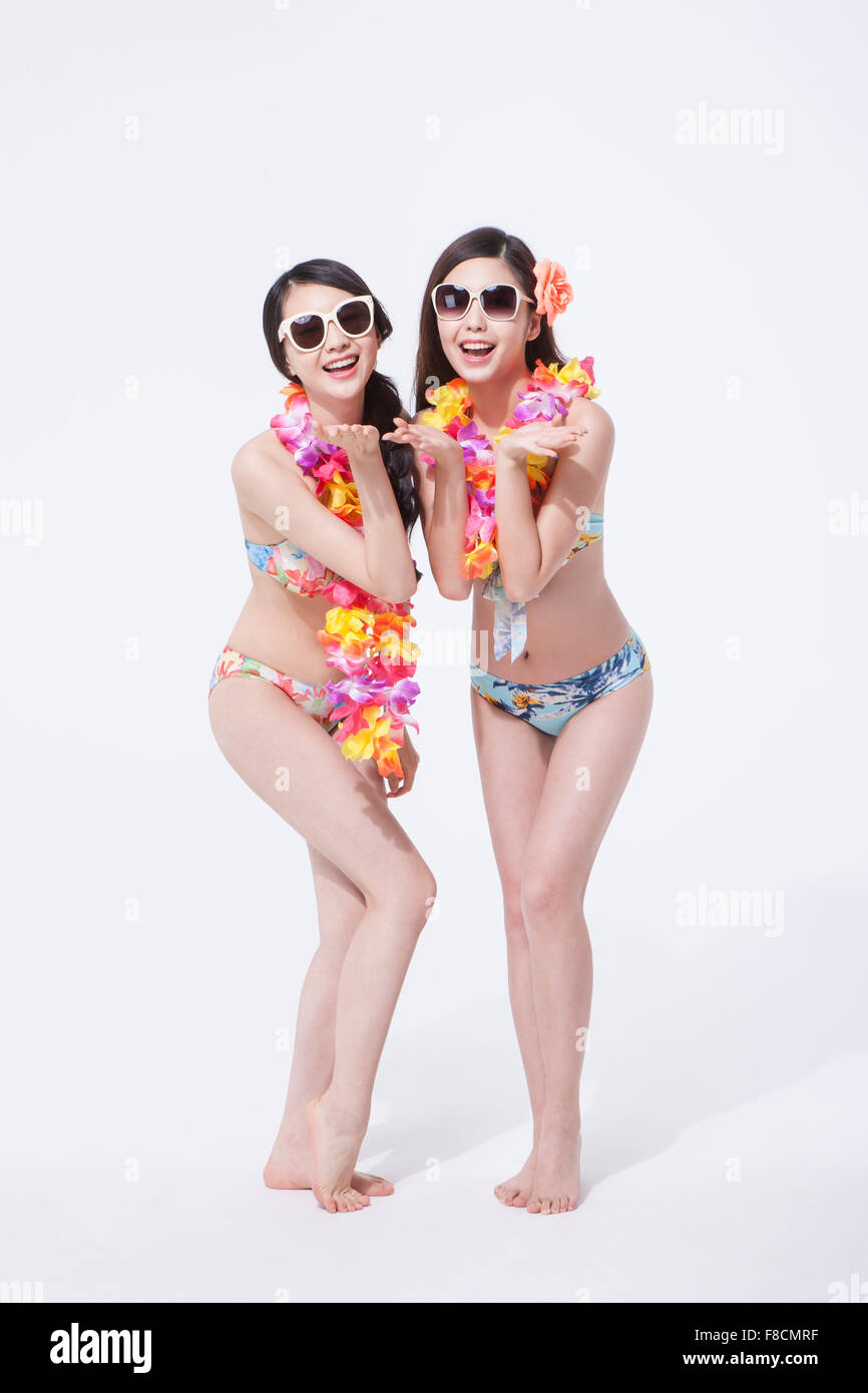 Zwei Frauen im Bikini und Blume Halskette tragen Sonnenbrillen stehen zusammen mit den Handflächen in der Nähe von ihrem Gesicht und Lächeln Stockfoto