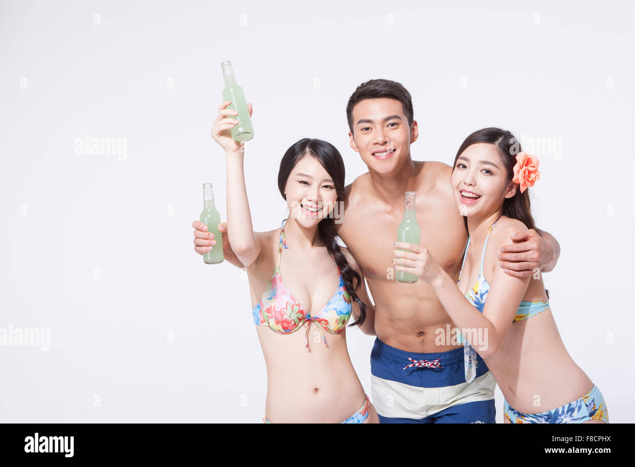 Mann im Schwimmen Hosen mit seinen Armen um zwei Frauen im Bikini, alle hält eine Flasche trinken jedes und lächelnd Stockfoto