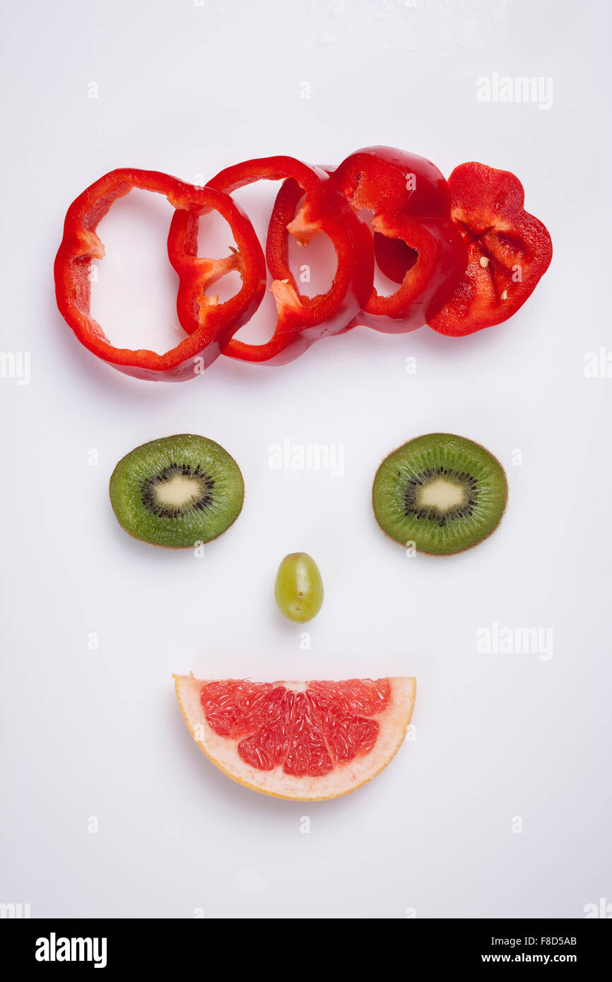 Essen Kunst machen lächelndes Gesicht gemacht mit grünen Kiwi, rote Paprika, grüne Traube und grapefruit Stockfoto