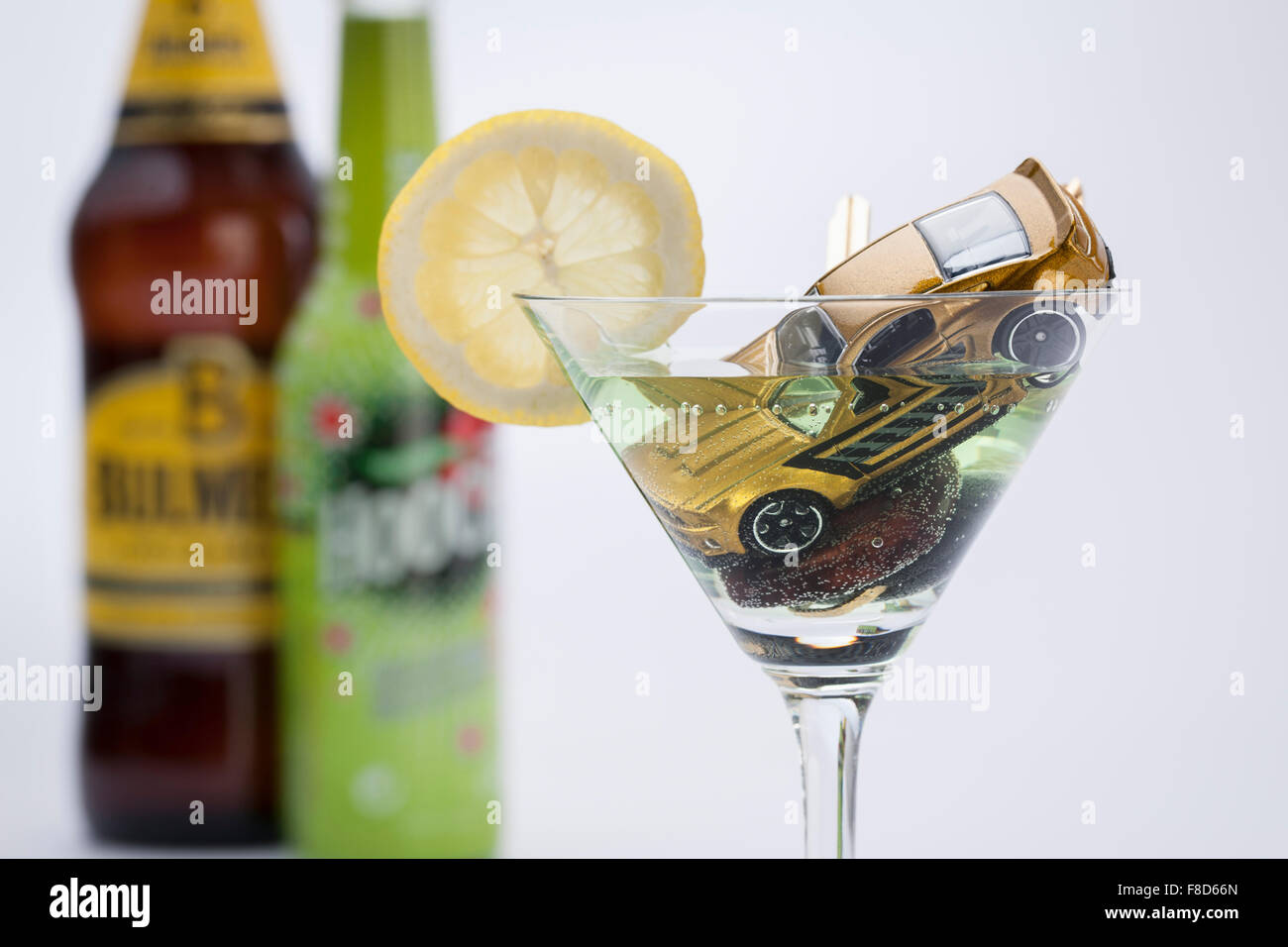 Miniatur-Autos und ein Autoschlüssel sinken nach unten in den Alkohol in ein Cocktailglas unscharf Stockfoto