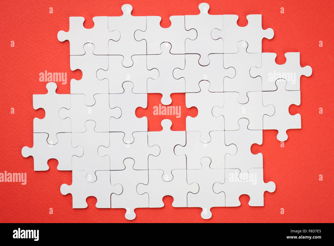 Gestell aus mit weißen Puzzleteile mit einem fehlenden Stück auf rotem Grund Stockfoto