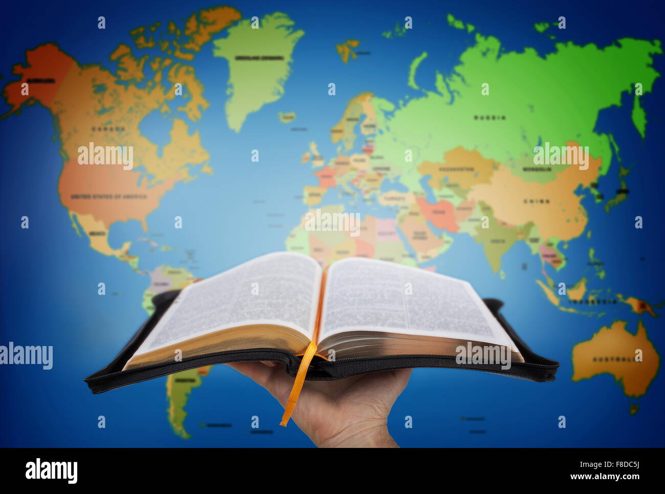 Hand zeigt die Heilige Bibel gegen Weltkarte Stockfoto