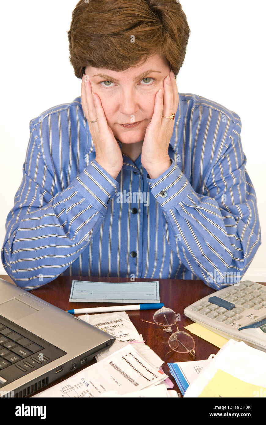Eine mittlere im Alter von Frau umgeben von ihrem Laptop, Scheckheft, Taschenrechner und Papierkram suchen finanziell überfordert. Stockfoto