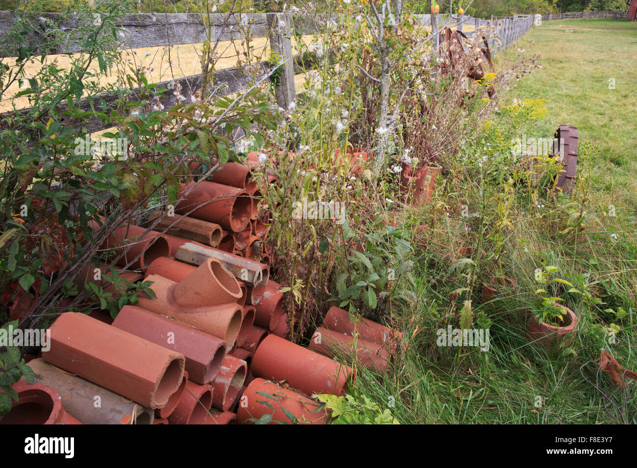 Alte Tonziegel Entwässerung gegen einen Zaun. Stockfoto Alte Tonziegel Entwässerung gegen einen Zaun. Stockfoto