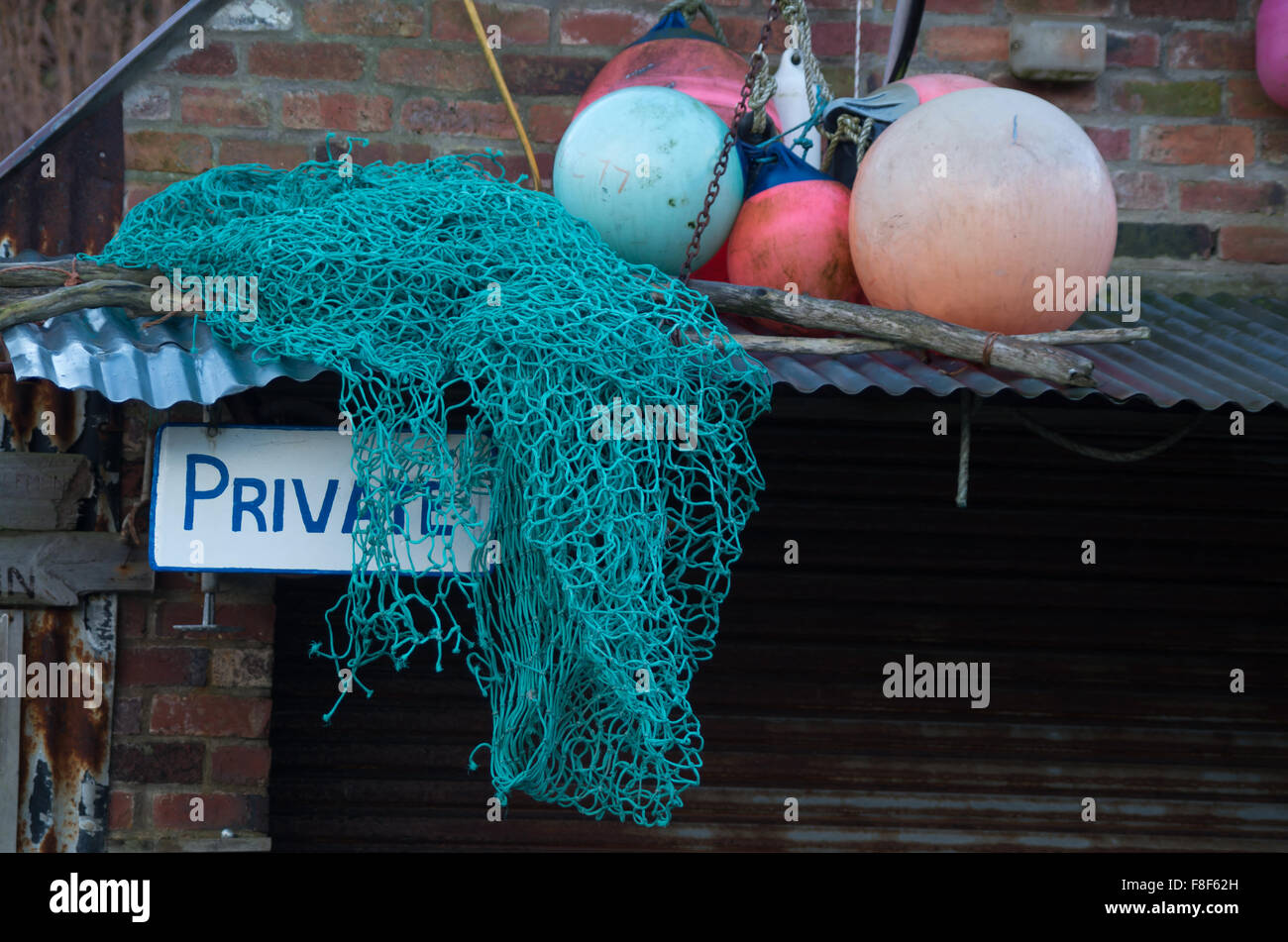 'Private' Schild mit Fischernetz und Bojen auf Blechdach. Stockfoto