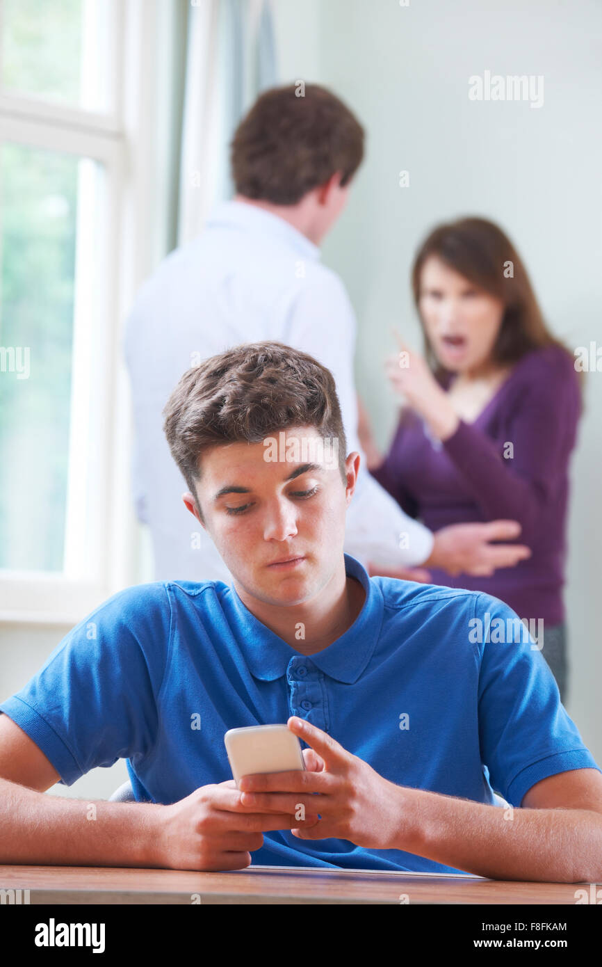 Teenager-Texte auf Handy als Eltern argumentieren im Hintergrund Stockfoto