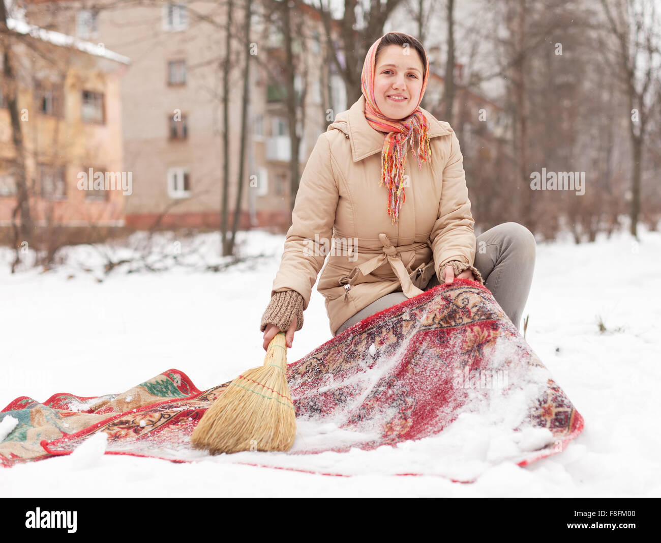 Russische Frau reinigt roten Teppich mit Schnee Stockfoto
