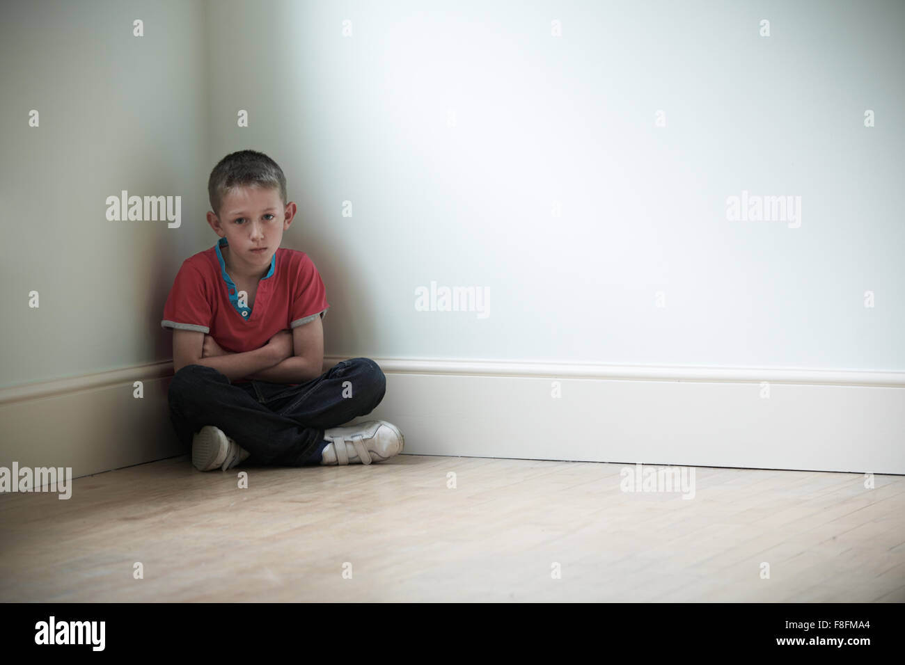 Unglückliches Kind sitzt In der Ecke des Raumes Stockfoto
