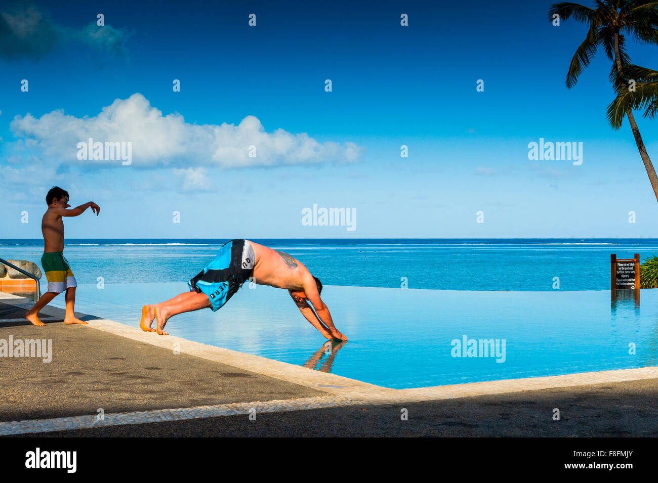 Ein Vater taucht in einem Infinity-pool, während sein Sohn Uhren auf der tropischen Insel der Fidschi-inseln im Südpazifik. Stockfoto