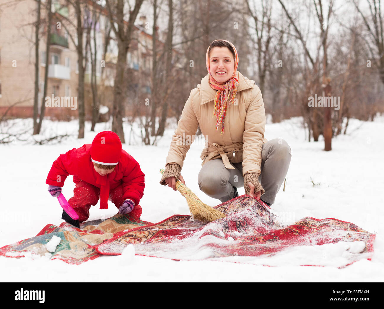 Frau mit Kind reinigt Teppich mit Schnee im Wintertag im freien Stockfoto