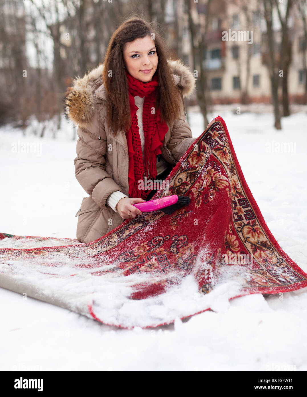Junge Frau reinigt Teppich mit Schnee im winter Stockfoto