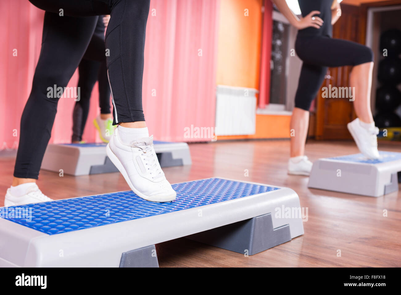 Nahaufnahme von Frau trägt weiße Turnschuhe tun Toe Tippen Sie auf Schritt-Plattform in Aerobic-Übungen Klasse mit Gruppe von Frauen im Hintergrund im Tanzstudio. Stockfoto