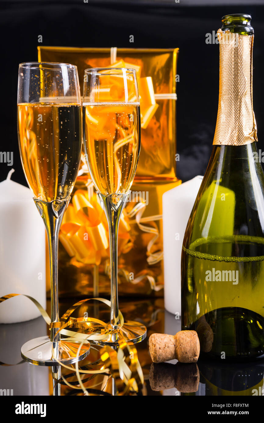 Nahaufnahme von entkorkt Flasche Champagner mit zwei gefüllten Gläsern in Still Life with Gold Weihnachtsgeschenke, weiße Kerzen und gewellten Band. Stockfoto