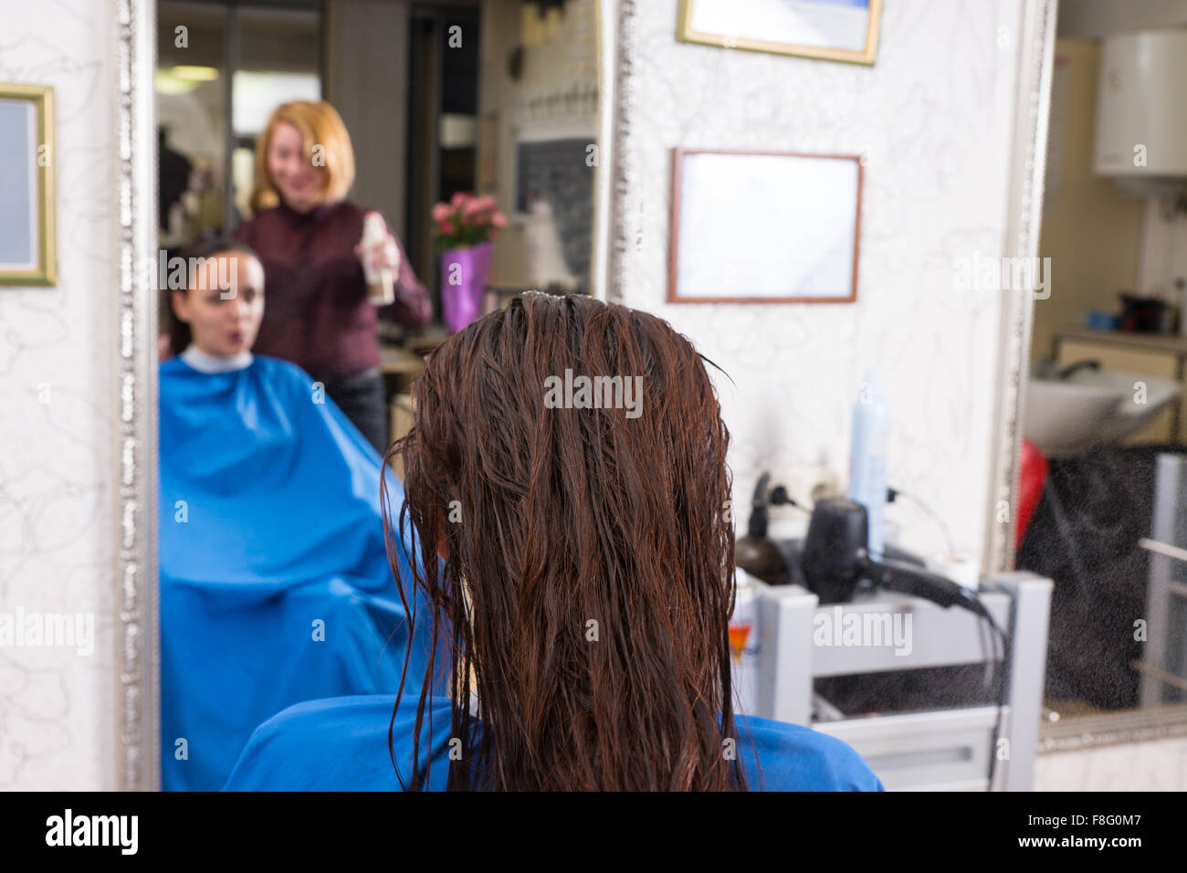 Rückansicht des Brünette Frau mit nassen Haaren im Stuhl im Salon mit Reflexion der Stylist und Frau im Spiegel im Hintergrund sitzen hautnah. Stockfoto