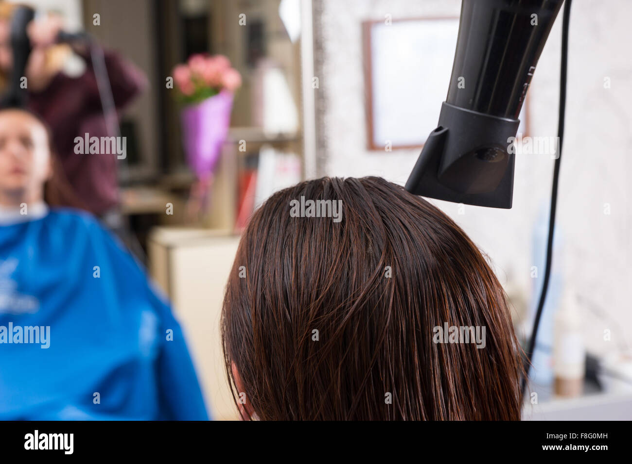 Rückansicht des Stylisten mit Fön trocknen nasses Haar Brünette Frau sitzt im Stuhl im Salon mit verschwommenen Spiegelbild im Hintergrund Spiegel hautnah. Stockfoto
