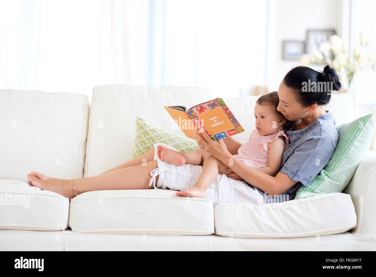 Mutter und Baby Tochter lesen auf sofa Stockfoto