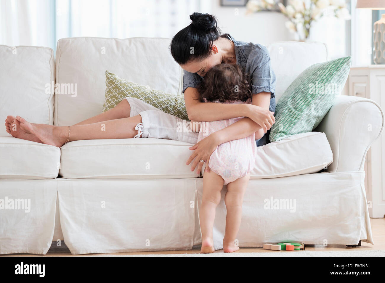 Mutter umarmt Baby-Tochter auf sofa Stockfoto